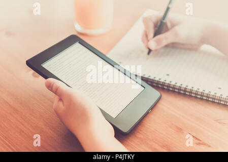 Girl is reading ebook on digital tablet device and is taking notes Stock Photo