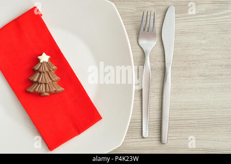 A simple place setting for Christmas consisting of a plate, fork, knife, red napkin and a chocolate shape christmas tree Stock Photo