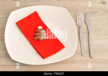 A simple place setting for Christmas consisting of a plate, fork, knife, red napkin and a chocolate shape christmas tree Stock Photo