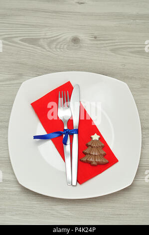 A simple place setting for Christmas consisting of a plate, fork, knife, red napkin and a chocolate shape christmas tree Stock Photo