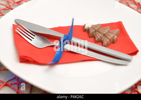 A simple place setting for Christmas consisting of a plate, fork, knife, red napkin and a chocolate shape christmas tree on a red place mat Stock Photo