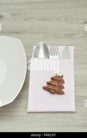 A simple place setting for Christmas consisting of a plate, fork, knife, white napkin and a chocolate shape christmas tree Stock Photo