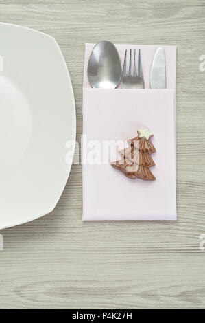 A simple place setting for Christmas consisting of a plate, fork, knife, white napkin and a chocolate shape christmas tree Stock Photo