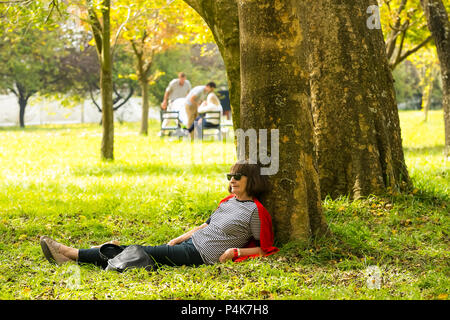 Johannesburg, South Africa, 05/10/2014, Middle aged lady lying against a tree at The Winter Sculpture Fair at Nirox Sculpture Park Stock Photo