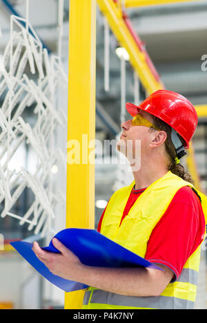 Factory supervisor in yellow reflective west with red helmet. Factory engineer checking production line holding blue folder with documents Stock Photo
