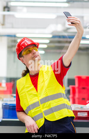 Worker in reflective west with red helmet taking selfie in a factory Stock Photo