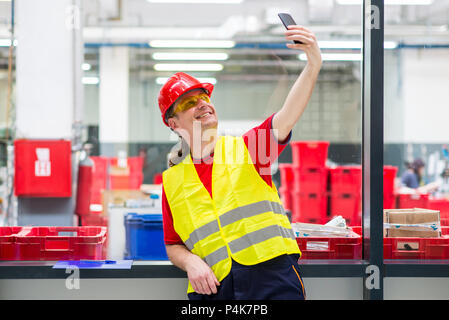 Worker in reflective west with red helmet taking selfie in a factory Stock Photo