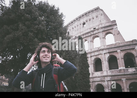 Vintage looking image of handsome young man with headphones listening to music in front of Colosseum in Rome Stock Photo