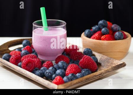 Milkshake in small glass cup with straw and surrounded by fresh beautiful juicy raspberries and blueberries Stock Photo