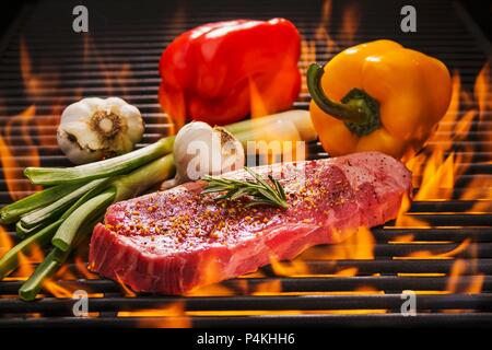 Beef steak with rosemary, red and yellow peppers, fresh garlic and spring onions on a flaming barbecue Stock Photo