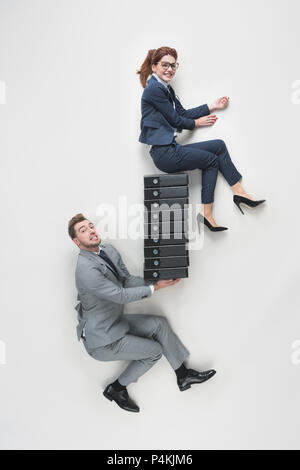 overhead view of businessman holding smiling businesswoman on pile of folders isolated on grey Stock Photo