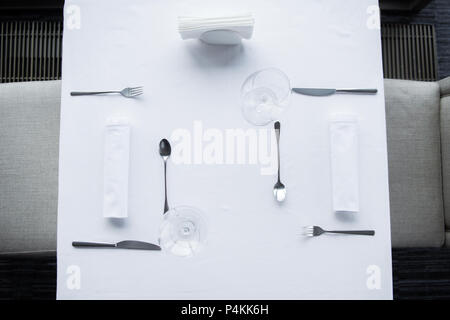 top view of arranged cutlery and wineglasses on table with white tablecloth in restaurant