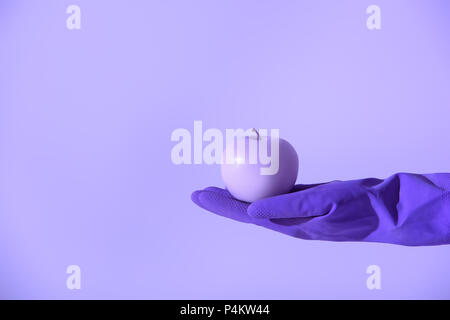 cropped view on hand in rubber glove holding purple apple, isolated on ultra violet Stock Photo