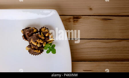 Walnuts and corn flakes covered in dark chocolate decorated with mint leaf on a wooden table Stock Photo