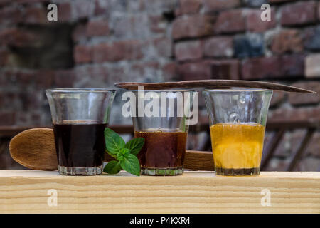 Three different types of honey in shot glasses arranged in a row o a piece of wood. Decorated with wooden spoons and a leaf of mint. Stock Photo