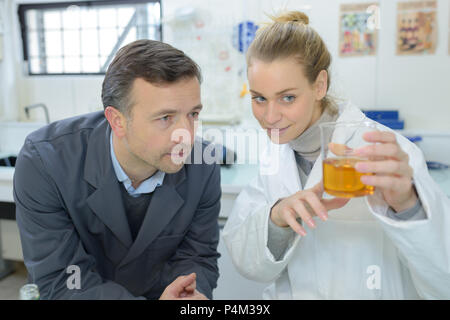 Technicians looking at yellow liquid in glass beaker Stock Photo