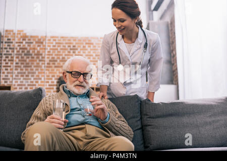 Doctor standing by senior man taking medications Stock Photo