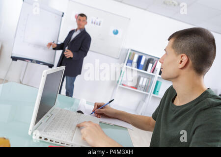 man stood at flipchart student sat using laptop making notes Stock Photo