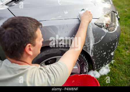 Young man washing his car with sponge