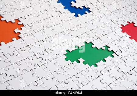 Close-up texture of a white jigsaw puzzle in assembled condition with missing elements, under which surfaces of different colors . Stock Photo