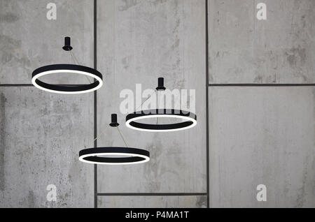 Unusual light sources hang on the background of a marble wall. Lamps in the form of a luminous ring . Stock Photo