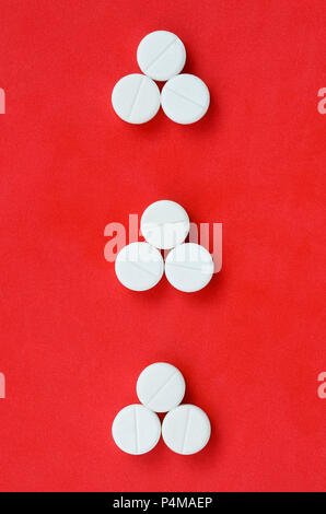 Several white tablets lie on a bright red background in the form of three triangular arrows. Background image on medicine and pharmaceutical topics . Stock Photo