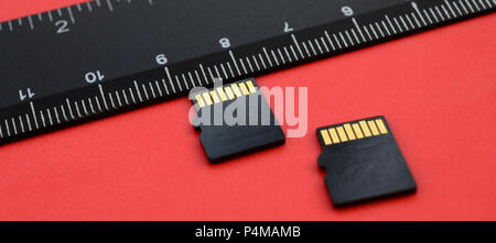 Two small micro SD memory cards lie on a red background next to a black ruler. A small and compact data and information store . Stock Photo