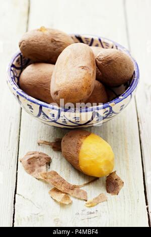 Potatoes cooked in their skins, in and next to a bowl Stock Photo