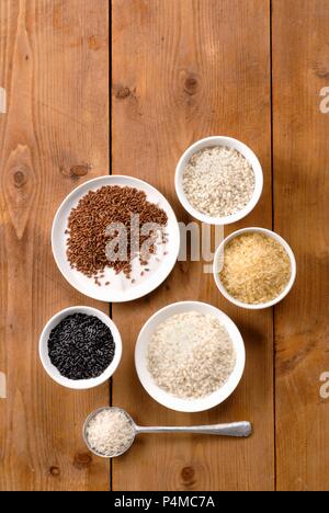 Various types of rice in bowls on wooden surface Stock Photo