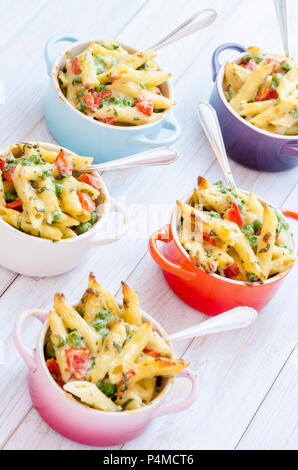 Mini servings of pasta bake with peas, cherry tomatoes in a creamy white sauce served in small colourful pots with forks Stock Photo