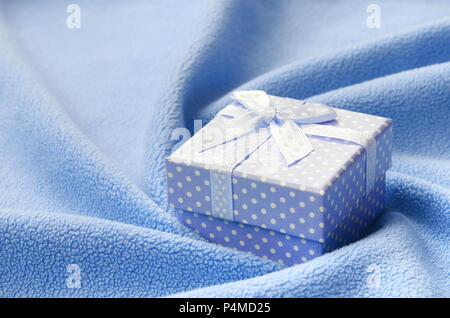 A small gift box in blue with a small bow lies on a blanket of soft and furry light blue fleece fabric with a lot of relief folds. Packing for a gift  Stock Photo