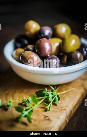 Green and black olives in a dish on a chopping board Stock Photo