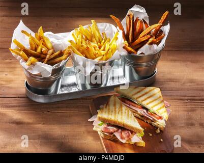 Three types of chips and a ham, cheese, tomato and lettuce sandwich on a rustic wooden table Stock Photo