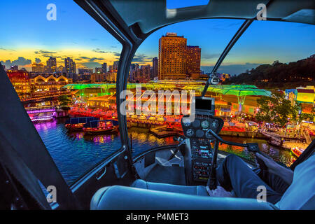 Helicopter cockpit interior flying on aerial skyline of Clarke Quay and riverside area at sunset in Singapore, Southeast Asia. Waterfront skyline on Singapore River. Popular nightlife attraction. Stock Photo