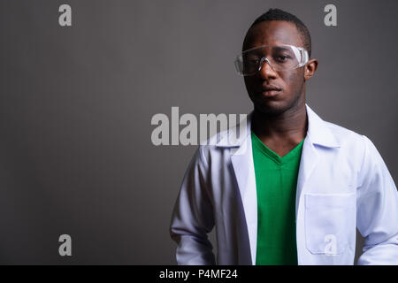 Young African man doctor wearing protective glasses against gray Stock Photo