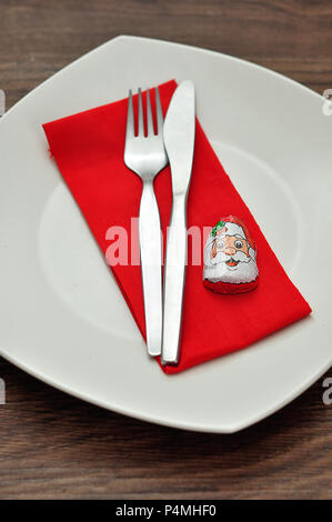 A simple place setting for Christmas consisting of a plate, fork, knife, red napkin and a chocolate wrapped with a Santa Clause's face Stock Photo