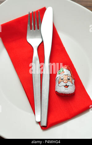 A simple place setting for Christmas consisting of a plate, fork, knife, red napkin and a chocolate wrapped with a Santa Clause's face Stock Photo