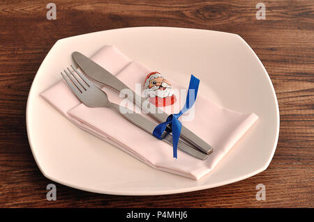 A simple place setting for Christmas consisting of a plate, fork, knife, white napkin and a chocolate wrapped with a Santa Clause's face Stock Photo