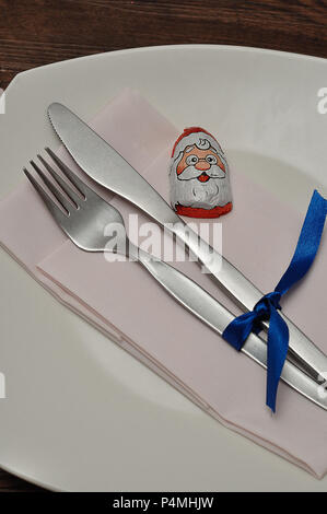 A simple place setting for Christmas consisting of a plate, fork, knife, white napkin and a chocolate wrapped with a Santa Clause's face Stock Photo