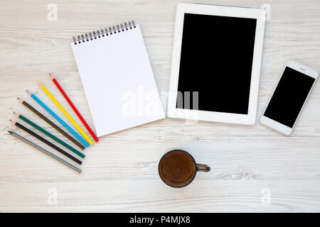 Feminine workspace with cup of coffee, smartphone, tablet, notebook, color pencils. Top view. Stock Photo