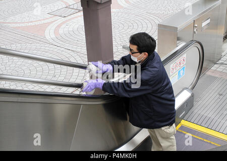 Unidentified person clean up a public escalator on а street in Tokyo. Man with rubber gloves clean up public place with mask. Person wear mask against Stock Photo