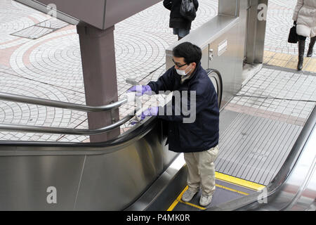 Unidentified person clean up a public escalator on а street in Tokyo. Man with rubber gloves clean up public place with mask. Person wear mask against Stock Photo