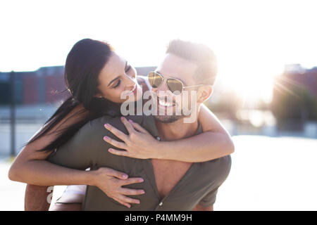 Happy young woman embracing stylish man from back outdoors in sunset Stock Photo