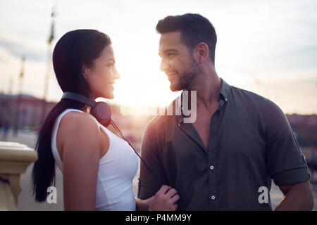 Happy young trendy couple dating in city sunset, looking to each other Stock Photo