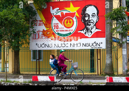 Woman riding a bicycle under an Vietnam Communist Party propaganda poster in Nam Dinh province, Vietnam - Propagandaplakat der kommunistischen Partei Vietnams in der Nam Dinh-Provinz, Vietnam Stock Photo