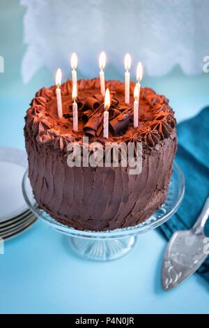 Chocolate birthday cake with 8 lit candles on cake stand Stock Photo