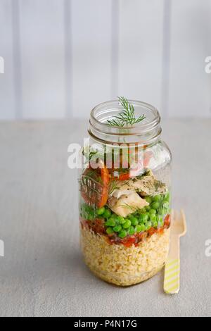 Couscous salad with fish, peas and tomatoes in a glass jar Stock Photo