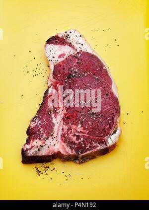 A raw T-bone steak seasoned with salt and pepper Stock Photo