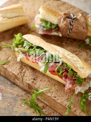 Rustic baguette with serrano ham, salami, rocket and tomato Stock Photo