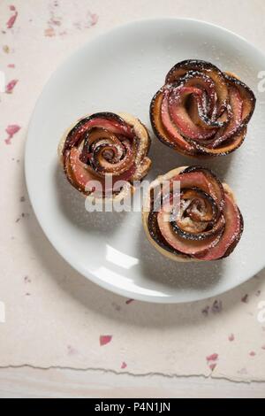 Three shortcrust apple roses on a white plate with icing sugar Stock Photo